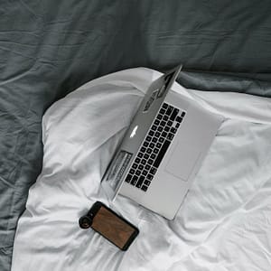 Billede af Laptop og mobiltelefon i en seng. Det kan påvirke din søvn negativt.
